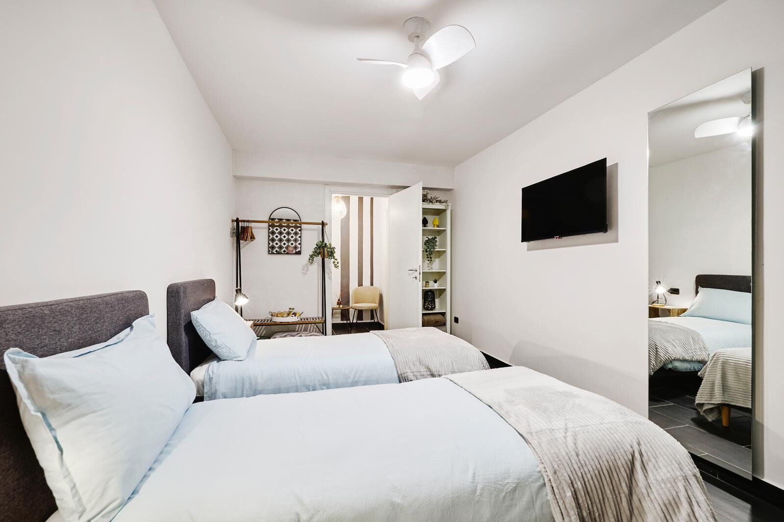 Une chambre moderne avec deux lits, une télévision, une armoire et un ventilateur de plafond.