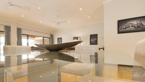 Un salon moderne avec une table basse en verre, des sièges confortables et des œuvres d’art accrochées aux murs.