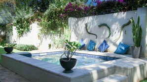 Une piscine bordée de pierres, un petit jardin avec des marches menant à un espace détente, et un mur agrémenté d’éléments décoratifs.