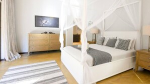 Une chambre à coucher avec un lit à baldaquin, une commode en bois, un téléviseur fixé au mur et un tapis à motifs.