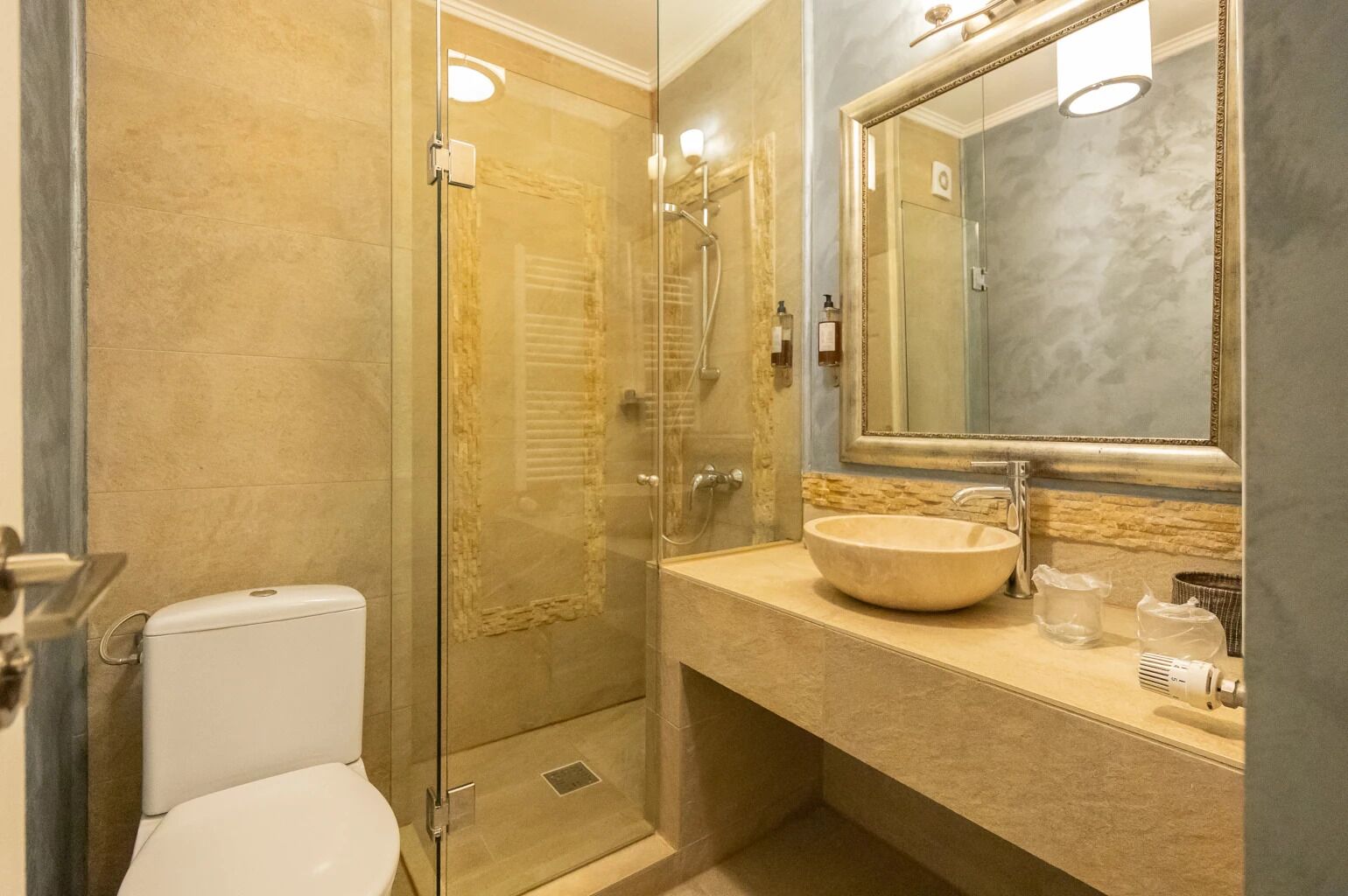 Un baño con ducha de vidrio, inodoro blanco, lavabo color beige y un espejo grande.