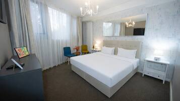 Een hotelkamer met een groot bed, een bureau met stoel, een kleine tafel met lamp, en een spiegel aan de muur.