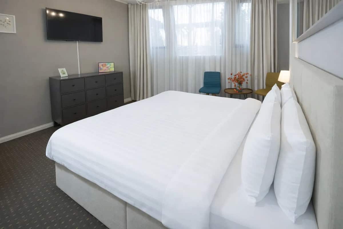 Een hotelkamer met een groot bed, een flatscreen televisie aan de muur, een tafeltje met een lamp en een stoel.