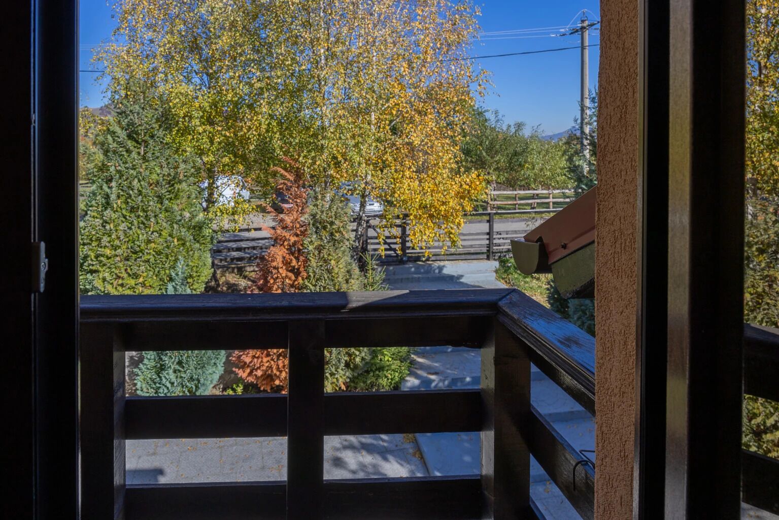 A view from a balcony with a railing, a tree with yellow leaves, and a clear sky.