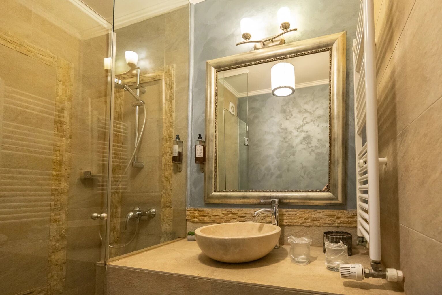 Ein Badezimmer mit einer Duschkabine, einem мраморной Waschbecken und einem großen Spiegel.
