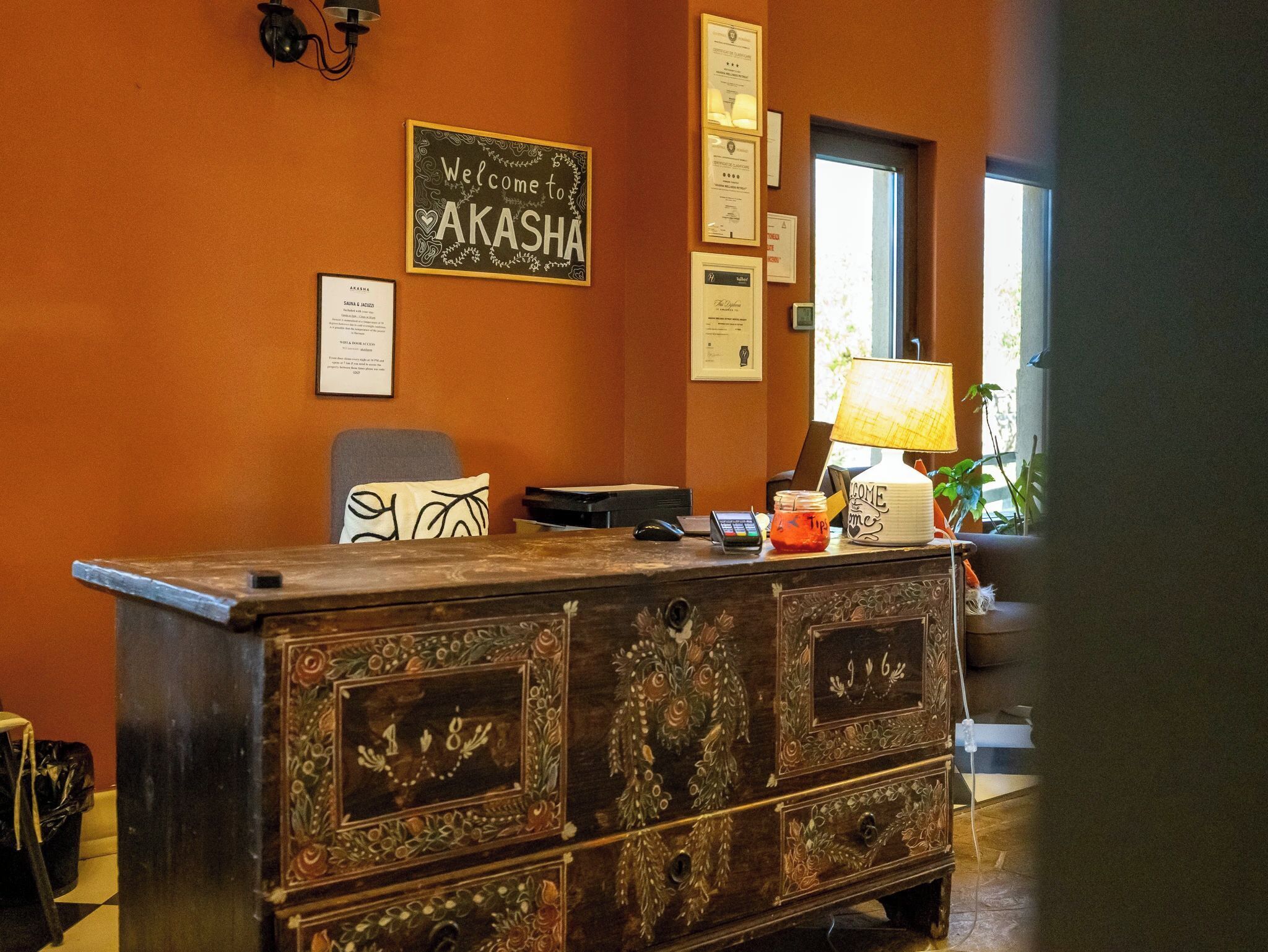 A reception desk with a sign reading 'Welcome to AKASHA,' a lamp, a phone, and framed certificates on the wall.