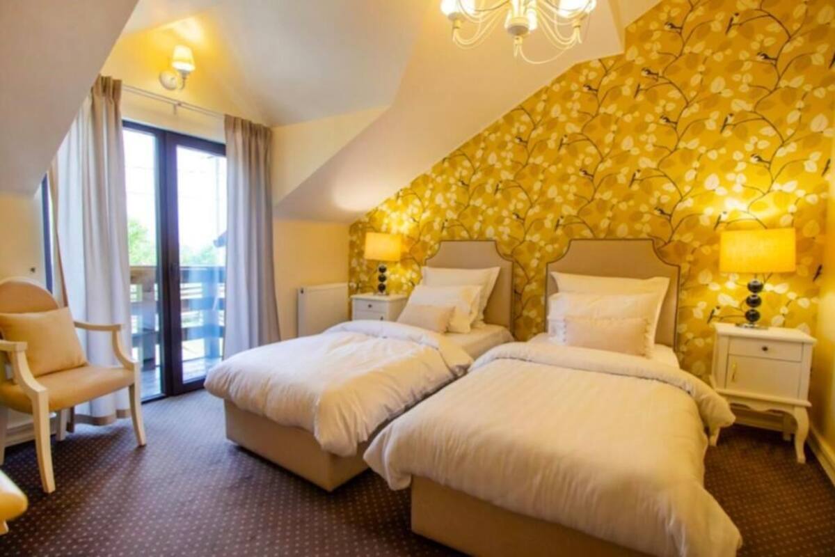 Een hotelkamer met twee bedden, een stoel, een balkon en een behang met een patroon.