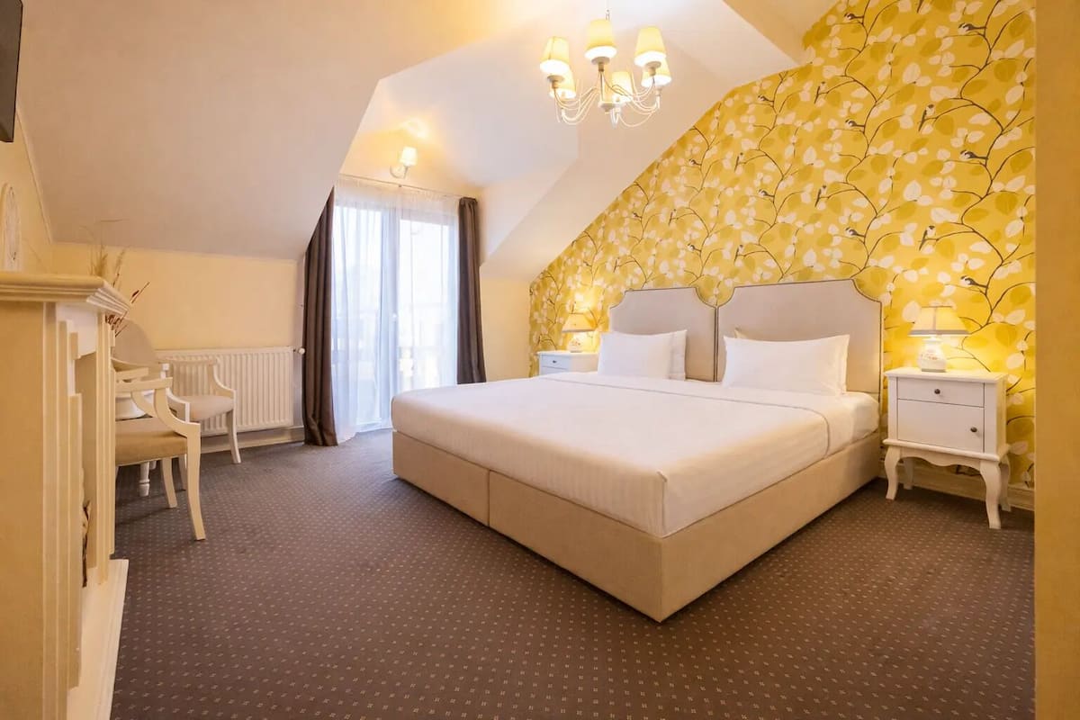 Een slaapkamer met een groot bed, een bureau en een stoel, een kroonluchter en een behang met een patroon.