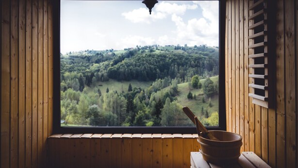 A wooden cabin room with a large window overlooking a forested landscape.