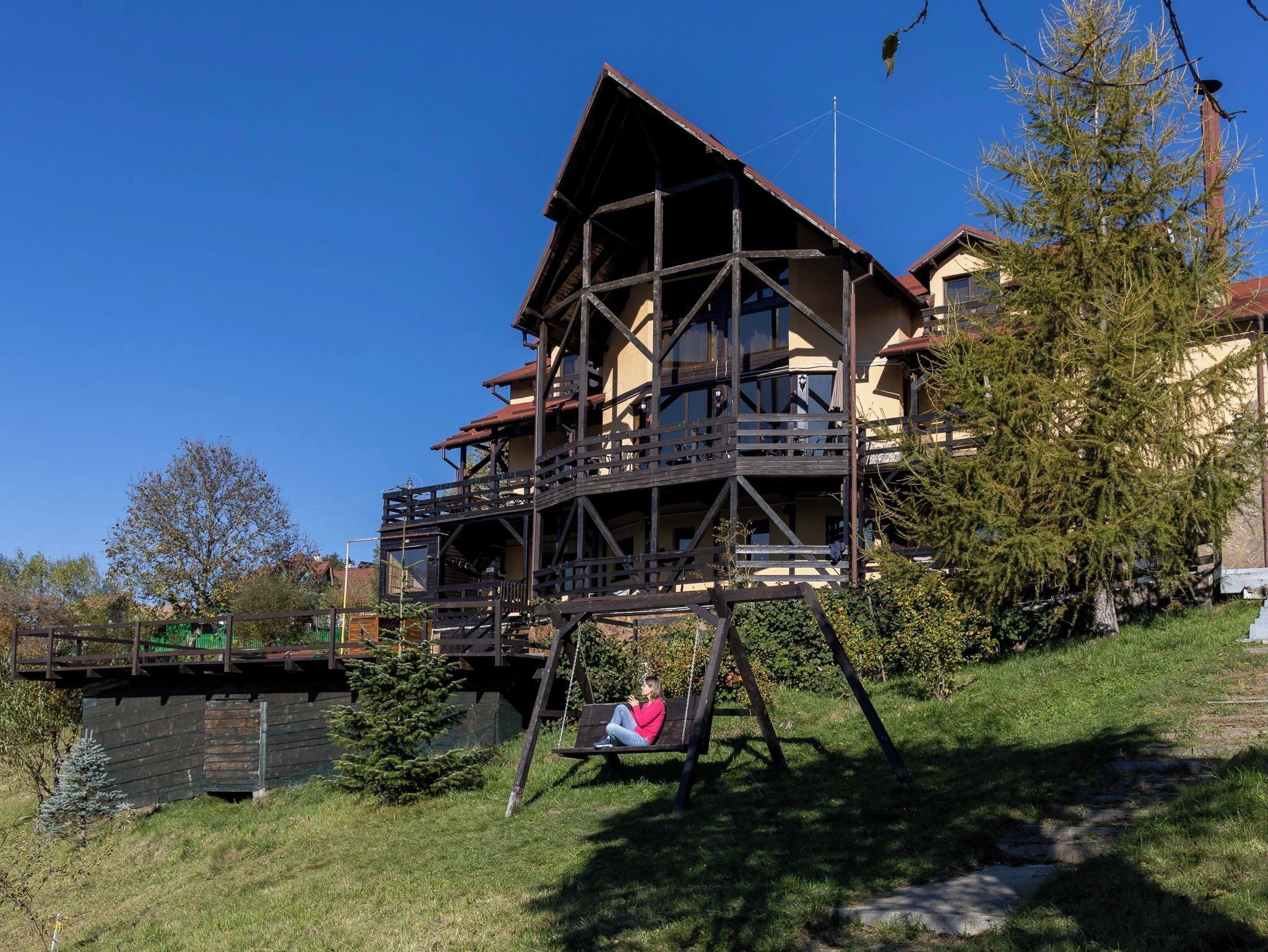 A chalet-style building with a wooden balcony, a swing, and a clear sky.