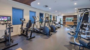 Une salle de sport moderne dotée de divers équipements pour le cardio et le renforcement musculaire, de grandes fenêtres et d’un intérieur propre et bien éclairé.