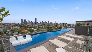 Une piscine sur le toit, dotée de chaises longues et offrant une vue panoramique sur la ville.