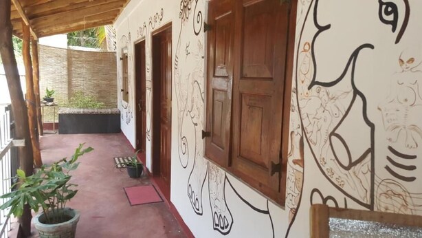 A covered outdoor area with a red mat, potted plants, and a wall with hand-drawn artwork. - Canoe Beach Resort (Tangalle)