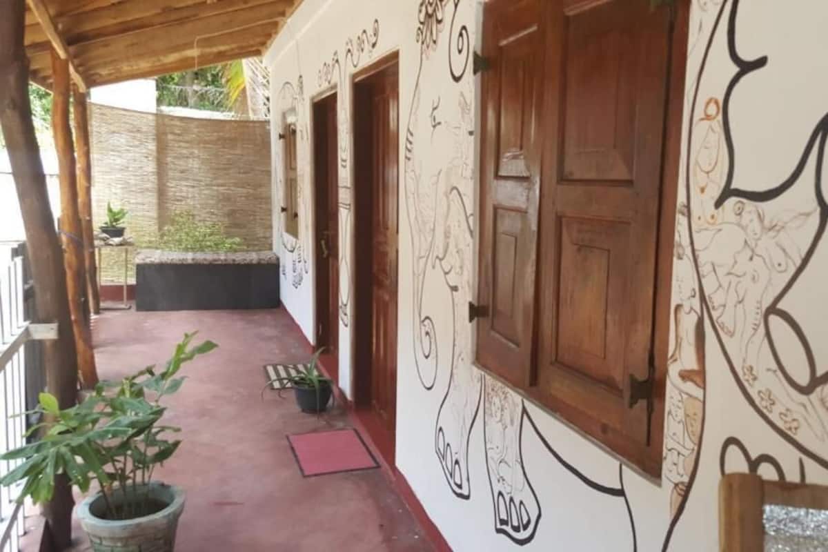 A covered outdoor area with a red mat, potted plants, and a wall with hand-drawn artwork.
