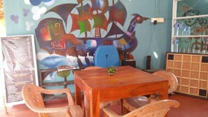 A dining area with a wooden table and chairs, a mural on the wall, and a menu board. - Canoe Beach Resort (Tangalle)