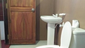 A bathroom with a wooden door, a white toilet, a sink, and a small mirror. - Canoe Beach Resort (Tangalle)