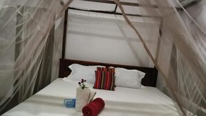 A bed with a canopy, white pillows, a striped pillow, a small vase with flowers, and a rolled towel. - Canoe Beach Resort (Tangalle)