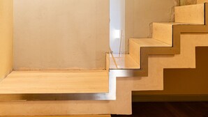 Una escalera con escalones de madera y baranda de vidrio, que conduce a una habitación con pared lisa y un panel decorativo.