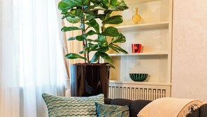 Una sala de estar con un sofá gris oscuro, una planta verde grande y una estantería con objetos decorativos.