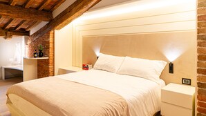 Un dormitorio con una cama grande, vigas de madera en el techo, una pared de ladrillo y lámparas de noche.