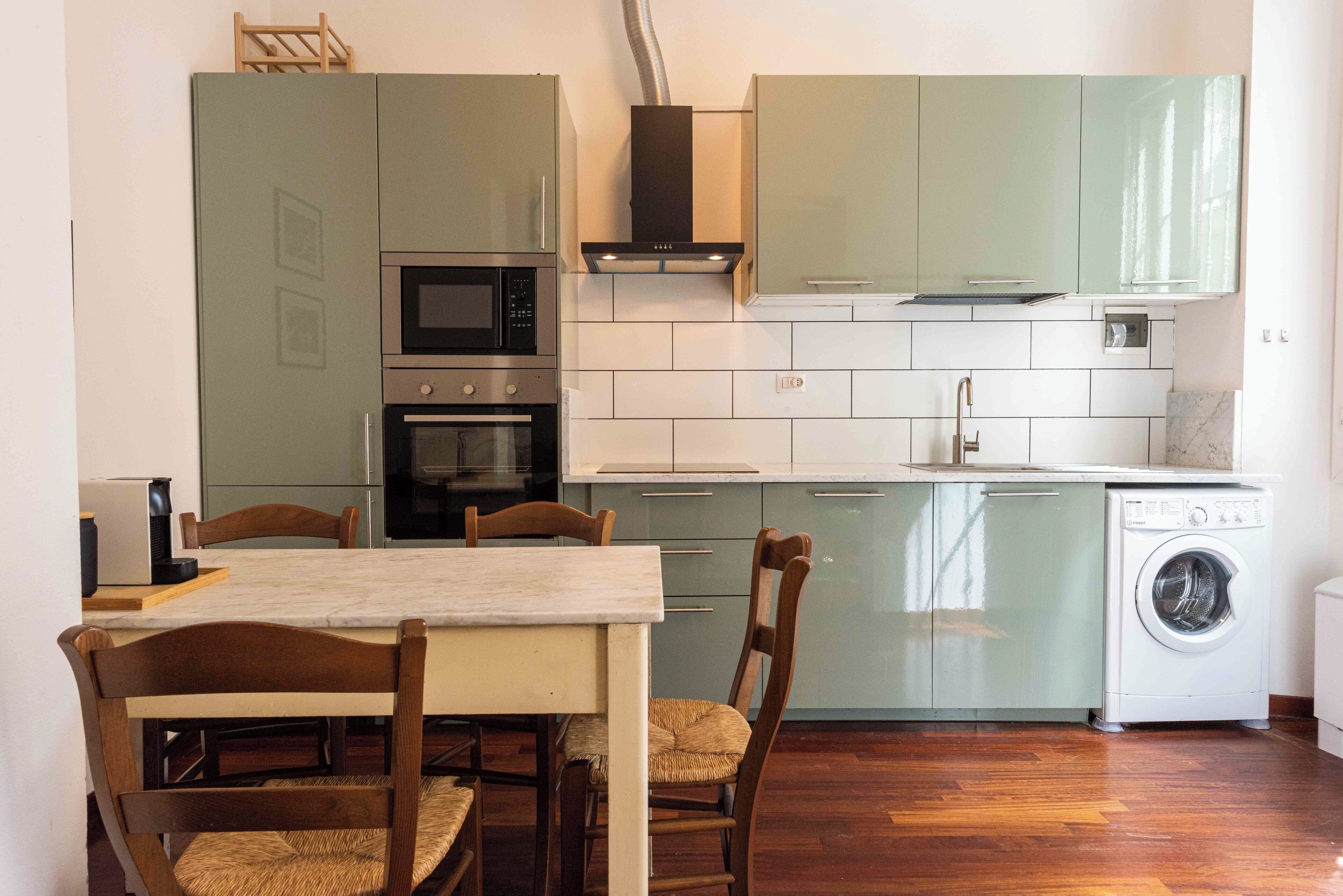 A compact kitchen with a dining area, including a table and chairs, a microwave, oven, and a washing machine.