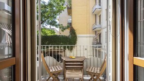 A balcony with a wooden table and two chairs, a small potted plant, and a view of the surrounding buildings. - Poliziano Apartment by Mmega (Florence)