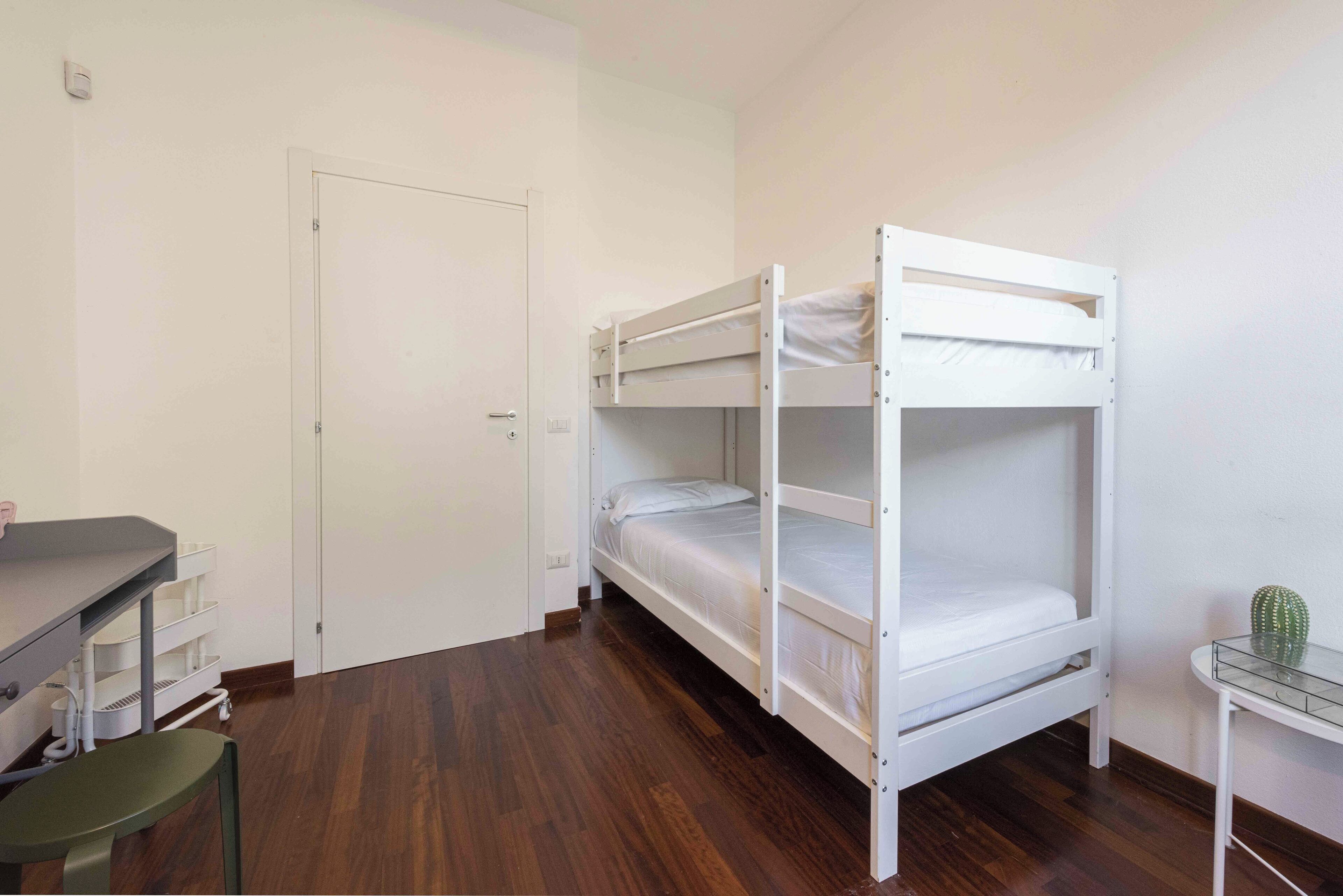 A bunk bed room with a desk and chair, a door, and a cactus on a small table.