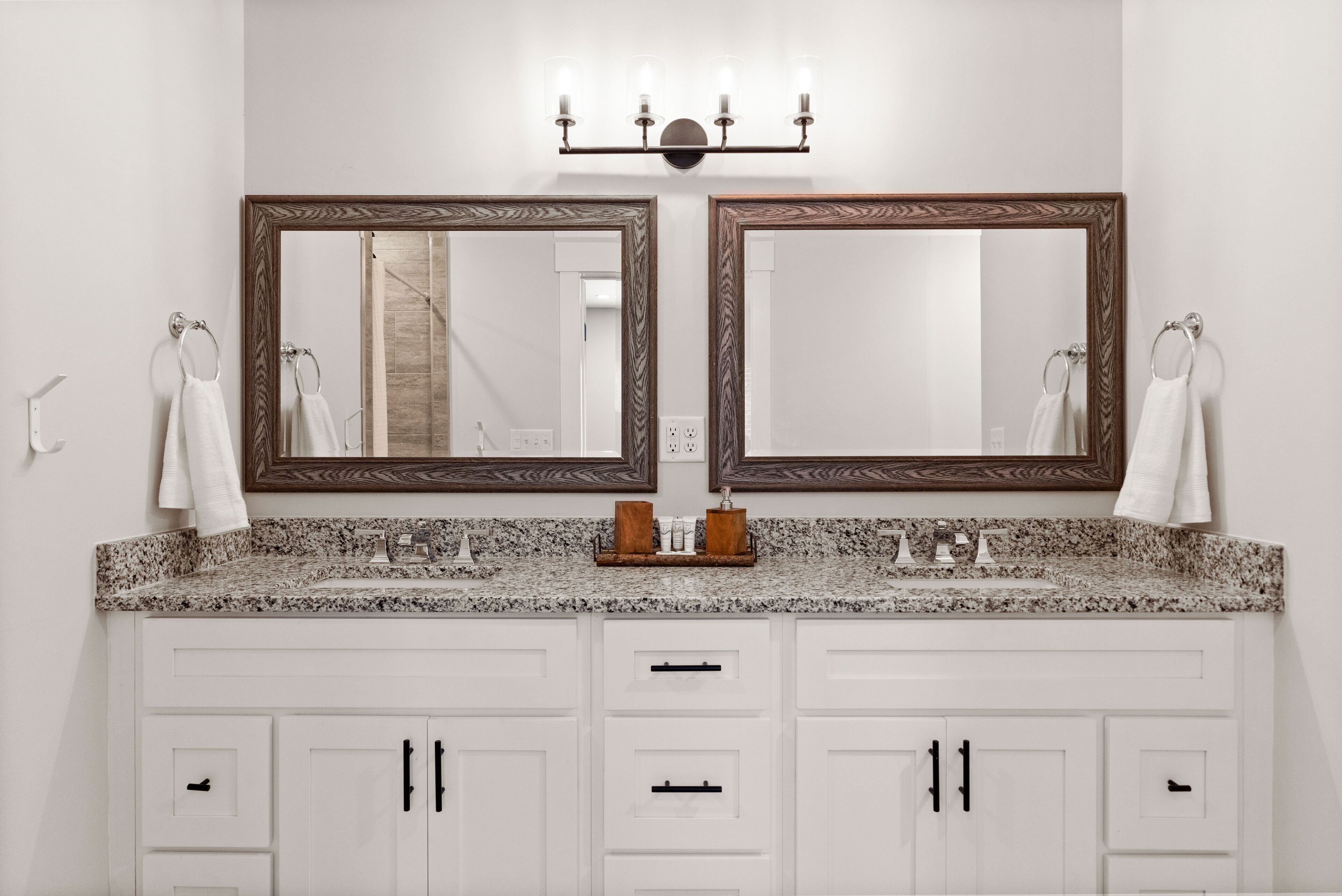 A bathroom with a double vanity, two mirrors, a granite countertop, and white cabinetry.