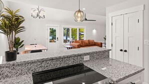 A modern kitchen with granite countertops, a built-in oven, and a dining area with a table and chairs. - Cape Fear Treehouse Boat Ramp, Dock, Kayaks, Firepit, Games (Pender County)