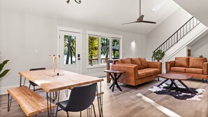 A spacious living area with a high ceiling, a dining table with benches, two sofas, a coffee table, and a chandelier. - Cape Fear Treehouse Boat Ramp, Dock, Kayaks, Firepit, Games (Pender County)