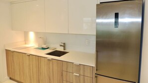 A modern kitchen with white cabinets, a stainless steel refrigerator, and a sink with a faucet. - Lux design 2 bedroom unit sleeps 6 in SoBe best area (Miami Beach)