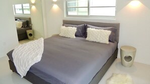 A modern bedroom with a large bed, a bedside table, a mirror, and a window with natural light. - Lux design 2 bedroom unit sleeps 6 in SoBe best area (Miami Beach)