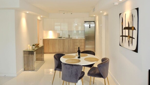 A modern kitchen with a central island, a dining area with a round table and chairs, and a minimalist art piece on the wall. - Lux design 2 bedroom unit sleeps 6 in SoBe best area (Miami Beach)