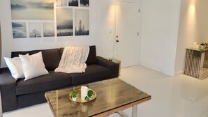 A modern living room with a dark sofa, a glass coffee table with decorative items, and a wall with framed artwork. - Lux design 2 bedroom unit sleeps 6 in SoBe best area (Miami Beach)