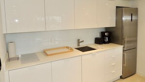 A modern kitchen with white cabinets, a stainless steel refrigerator, a sink, and a coffee maker.