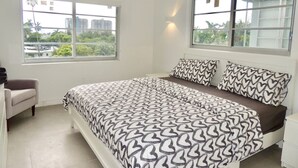 A bedroom with a large bed, a chair, and a window with a view of buildings and greenery.