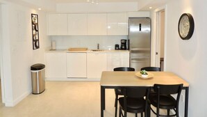 A modern kitchen with white cabinets, a stainless steel refrigerator, and a dining area with a wooden table and black chairs.