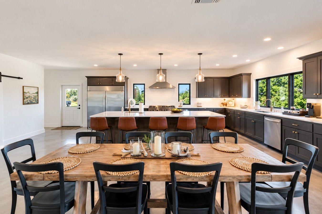 Una cocina moderna con una isla central, iluminación colgante y un comedor con mesa y sillas de madera.