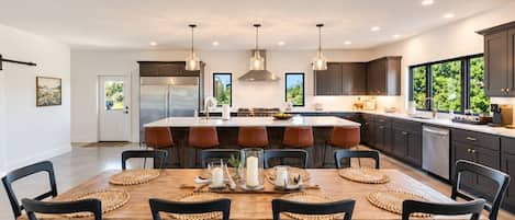 Una cocina moderna con una isla central, iluminación colgante y un comedor con mesa y sillas de madera.