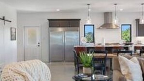 Una sala moderna con sofá, sillón y mesa de centro. Cuenta con una zona de cocina con mesa y sillas.