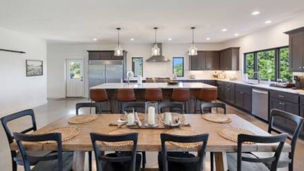 Una cocina moderna con una isla central, iluminación colgante y un comedor con mesa y sillas de madera.