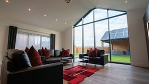 A spacious living room with a large window, a black leather sofa set, and a red rug. - Northumberland Luxury Stays - The Shearling (Morpeth)