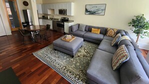 Een moderne woonkamer met een grijze modulaire bank, een eettafel met stoelen, een keukenhoek en een kamerbreed tapijt met een patroon.