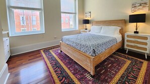 Een slaapkamer met een houten bed, twee nachtkastjes, een plafondventilator en een groot raam.