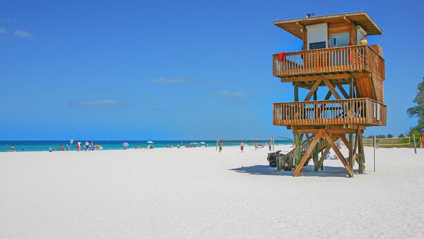 Una torre de salvavidas de madera en una playa con cielos azules despejados.