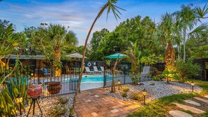 Un área de piscina con terraza de baldosas, palmeras y sillas de descanso.