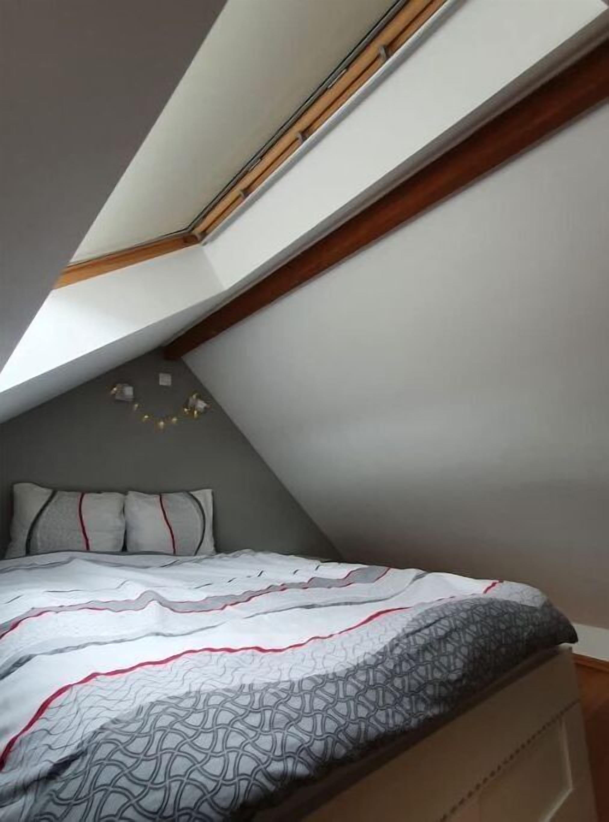 Een slaapkamer met een schuine plafond, een bed met behang en een klein wandlampje.
