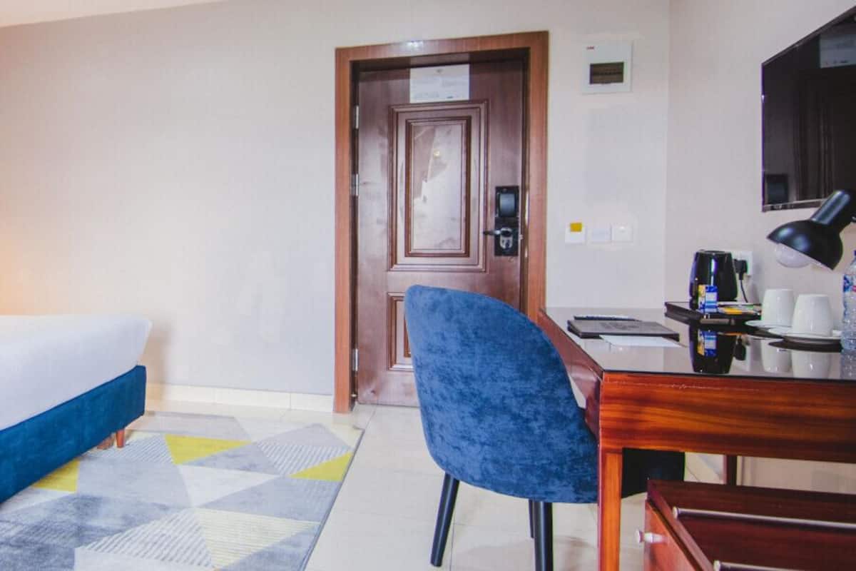 A hotel room with a bed, a desk with a chair, a desk lamp, a coffee maker, and a television.