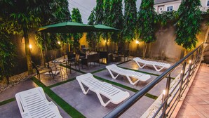 An outdoor patio with lounge chairs, tables, and umbrellas. - White Stones Hotel (Port Harcourt)