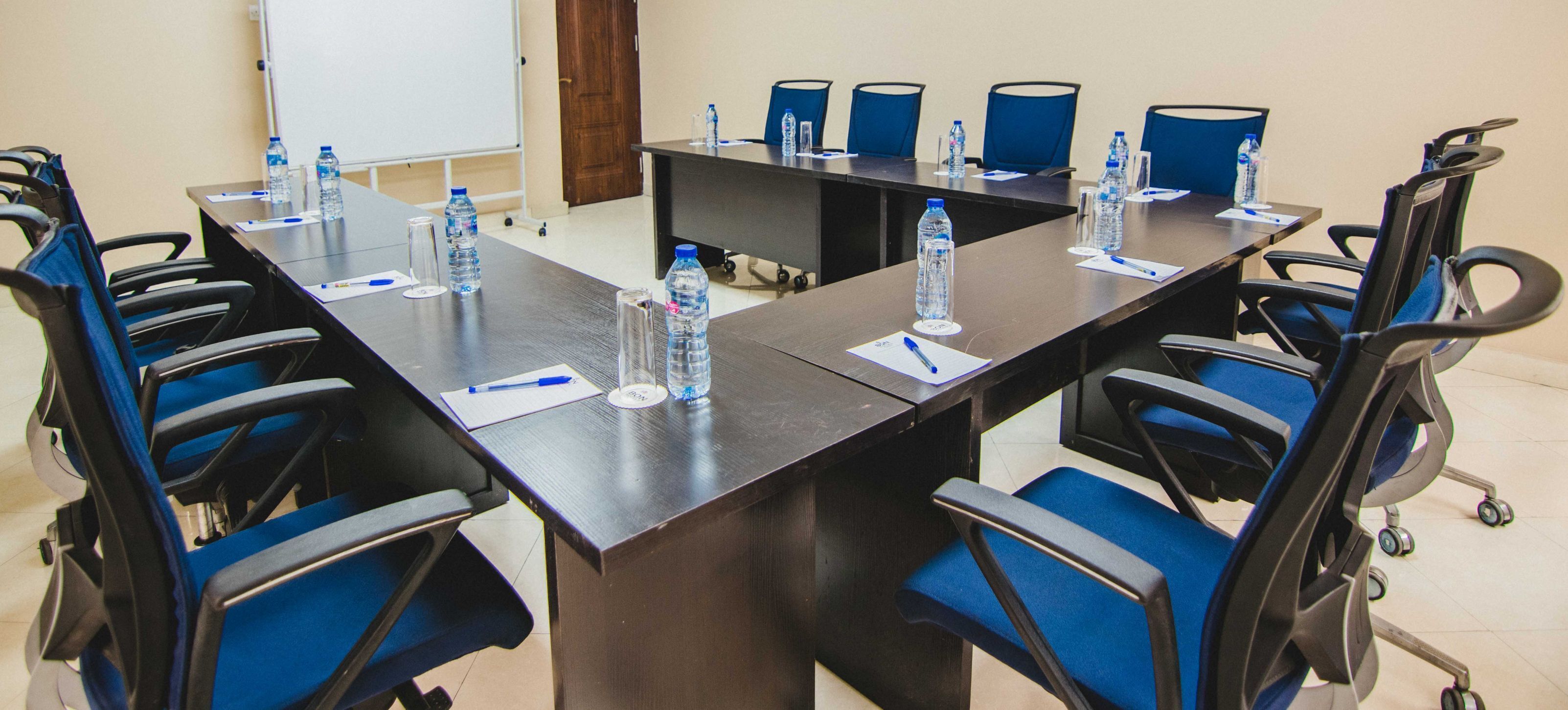 A conference room with a long table, blue chairs, water bottles, and papers.